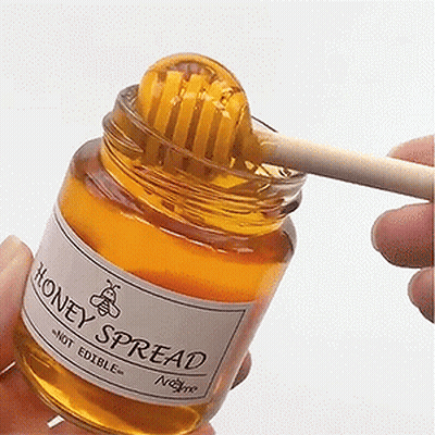 A Person Is Holding A Jar Of Honey Spread With A Honey Dipper In It GIF