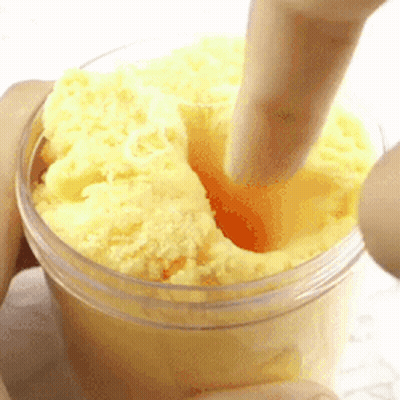 A Person Is Holding A Jar Of Yellow Slime With A Spoon . GIF