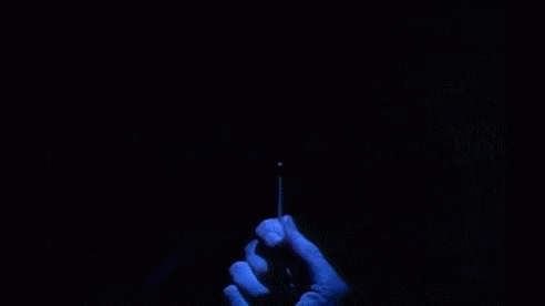 A Person Is Holding A Lighter In Front Of A Sign That Says `` Are You Afraid Of The Dark '' . GIF
