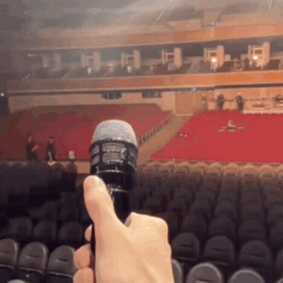 A Person Is Holding A Microphone In Front Of A Large Auditorium GIF