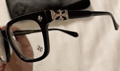 A Person Is Holding A Pair Of Glasses With A Cross On The Lenses . GIF
