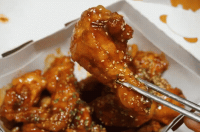 A Person Is Holding A Piece Of Chicken With Chopsticks GIF