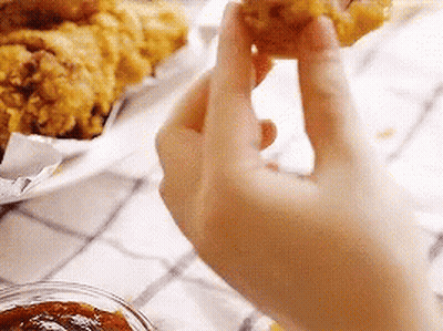 A Person Is Holding A Piece Of Fried Chicken . GIF