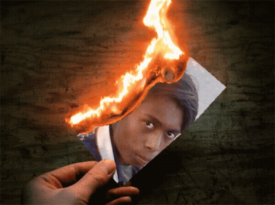 A Person Is Holding A Piece Of Paper That Is On Fire GIF