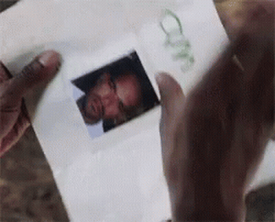 A Person Is Holding A Piece Of Paper With A Picture Of A Man 'S Face On It GIF