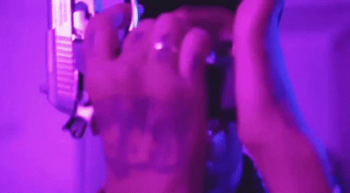 A Person Is Holding A Purple Object In Their Hands In A Purple Light . GIF