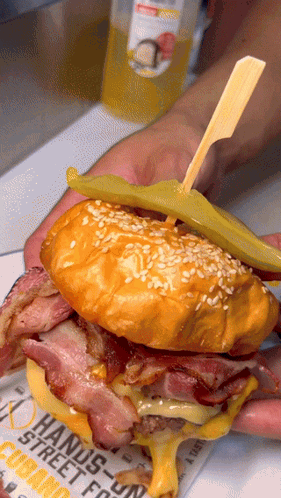 A Person Is Holding A Sandwich With A Pickle On A Newspaper That Says " Hands-On " GIF