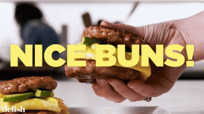 A Person Is Holding A Sandwich With The Words Nice Buns Behind Them GIF
