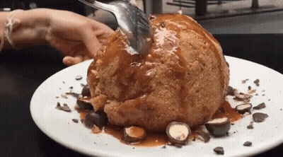 A Person Is Holding A Spoon Over A Dessert On A Plate . GIF