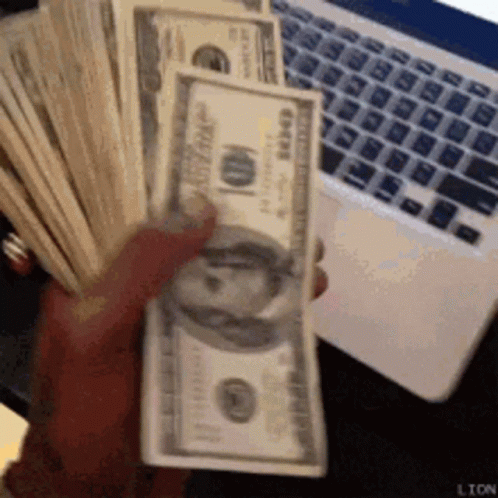 A Person Is Holding A Stack Of 100 Dollar Bills In Front Of A Laptop . GIF