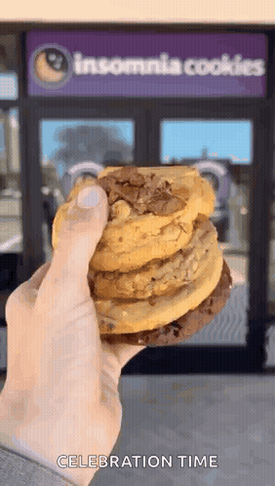 A Person Is Holding A Stack Of Cookies In Front Of A Insomnia Cookies Store GIF