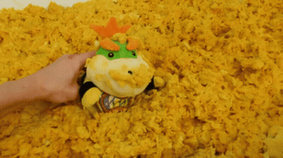 A Person Is Holding A Stuffed Animal In A Pile Of Yellow Popcorn GIF