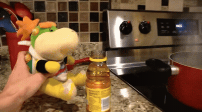 A Person Is Holding A Stuffed Animal In Front Of A Stove With A Bottle Of Cooking Oil Next To It GIF