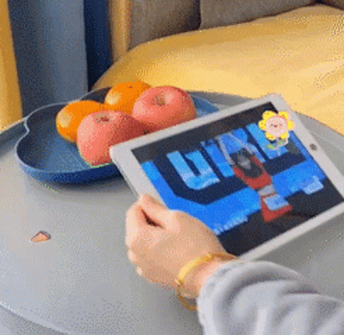 A Person Is Holding A Tablet In Front Of A Tray Of Apples And Oranges GIF