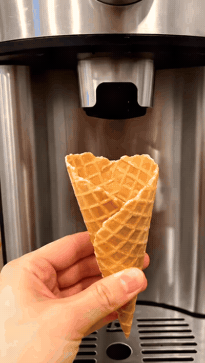A Person Is Holding A Waffle Cone In Front Of A Coffee Machine GIF