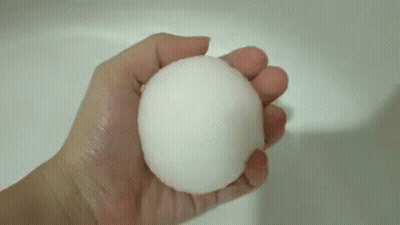 A Person Is Holding A White Ball In Their Hand Over A Sink . GIF