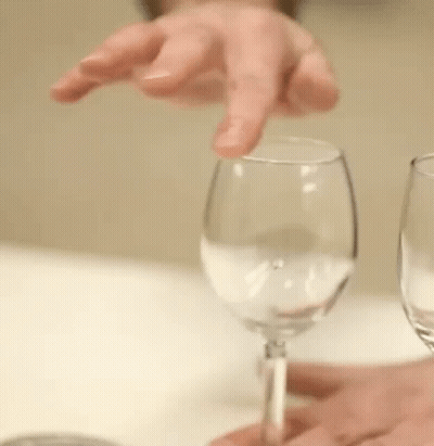 A Person Is Holding A Wine Glass With Their Finger And A Wine Glass With A Straw In It . GIF