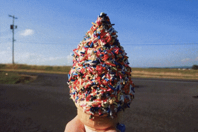 A Person Is Holding An Ice Cream Cone With Sprinkles On It GIF