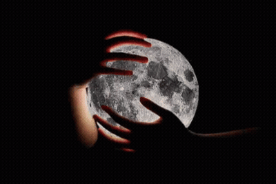 A Person Is Holding The Full Moon In Their Hands In The Dark . GIF