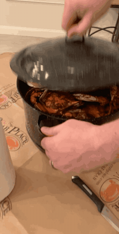 A Person Is Holding The Lid Of A Pot Of Crabs On A Table GIF