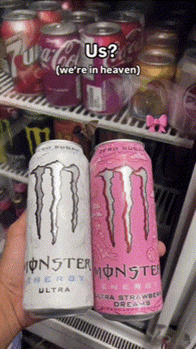 A Person Is Holding Two Cans Of Monster Energy Drinks In Front Of A Fridge GIF