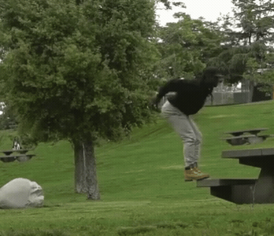 A Person Is Jumping In The Air Near A Picnic Table In A Park GIF