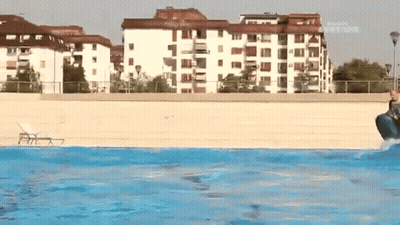 A Person Is Jumping Into A Swimming Pool With A Building In The Background That Says ' Allianz ' GIF