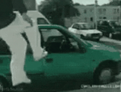 A Person Is Jumping Out Of A Green Car On A Street GIF