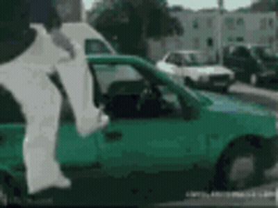 A Person Is Jumping Out Of A Green Car With A White Shirt On . GIF