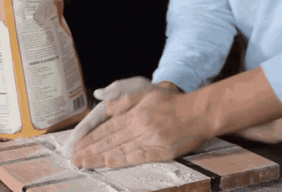A Person Is Kneading A Dough On A Cutting Board With A Box Of Flour In The Background GIF
