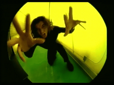 A Person Is Kneeling Down In Front Of A Yellow Wall And Making A Hand Gesture . GIF