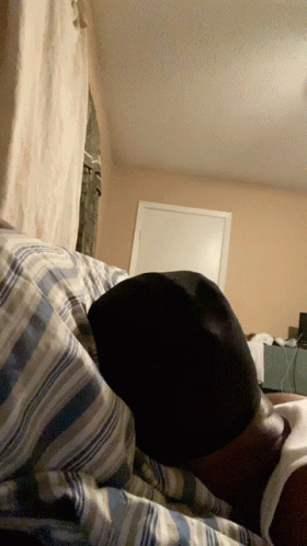 A Person Is Laying On A Bed With A Hat On Their Head GIF