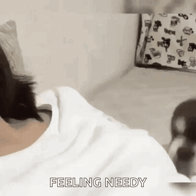 A Person Is Laying On A Bed With The Words `` Feeling Needy '' Written On The Bottom Of Their Shirt . GIF