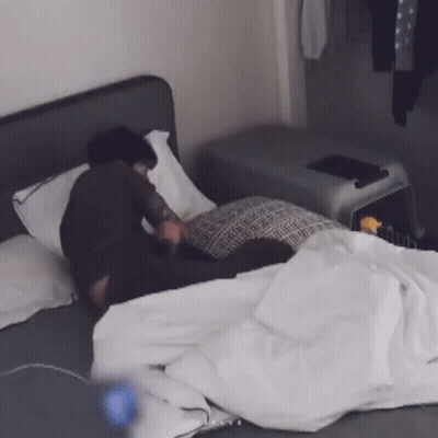 A Person Is Laying On A Bed With White Sheets And Pillows GIF