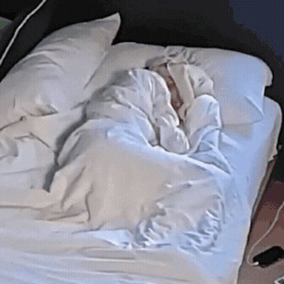 A Person Is Laying On A Bed With White Sheets GIF