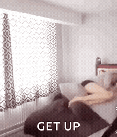 A Person Is Laying On A Couch In A Bedroom With The Words `` Get Up '' Written On It . GIF