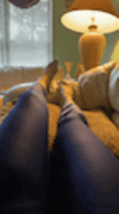 A Person Is Laying On A Couch With Their Feet Up In Front Of A Lamp . GIF