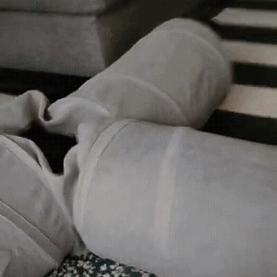A Person Is Laying On A Couch With Their Legs Crossed And A White Pillow On Top Of Them . GIF