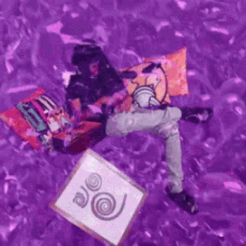 A Person Is Laying On A Purple Surface Holding A Picture And A Pillow . GIF