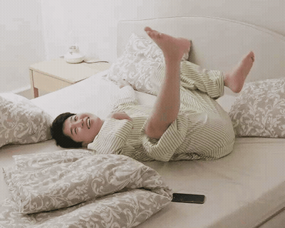 A Person Is Laying On Their Back On A Bed With Their Legs Up GIF