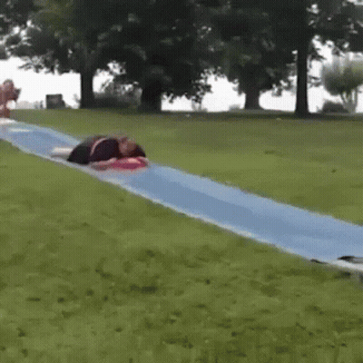 A Person Is Laying On Top Of A Blue Water Slide In A Park . GIF