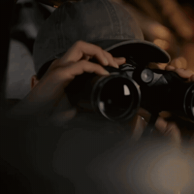 A Person Is Looking Through Binoculars With A Hat On GIF