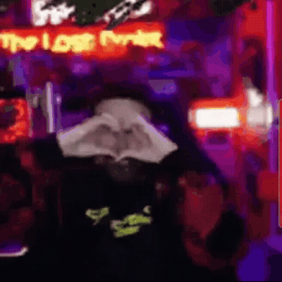 A Person Is Making A Heart Shape With Their Hands In Front Of A Neon Sign That Says `` The Lost Ever '' . GIF
