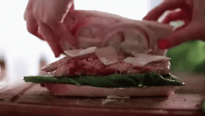 A Person Is Making A Sandwich With Chicken , Lettuce , Cheese And Onions On A Cutting Board . GIF