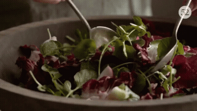 A Person Is Mixing A Salad In A Wooden Bowl With The Number 52 On The Bottom Right GIF