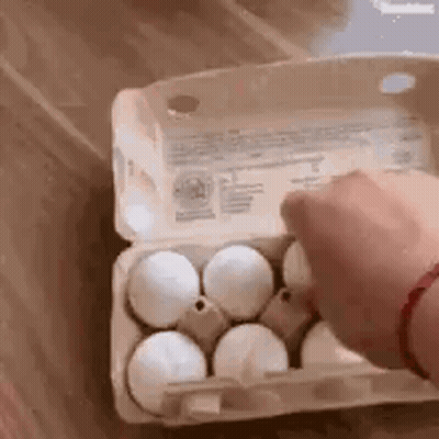 A Person Is Opening A Carton Of Eggs On A Table . GIF