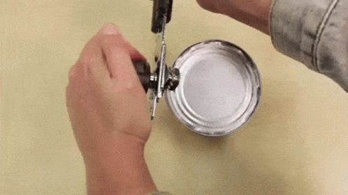 A Person Is Opening A Tin Can With A Can Opener . GIF