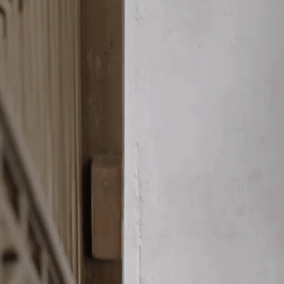 A Person Is Peeking Out From Behind A Wall And Looking At Something . GIF