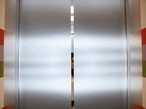 A Person Is Peeking Through A Sliding Glass Door In An Elevator GIF