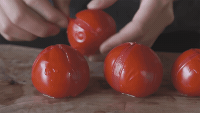 A Person Is Peeling Three Tomatoes On A Wooden Table GIF